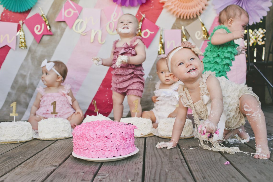 Cute baby girls with birthday cakes on floorboard at party