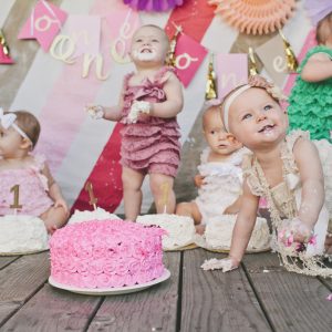 Cute baby girls with birthday cakes on floorboard at party